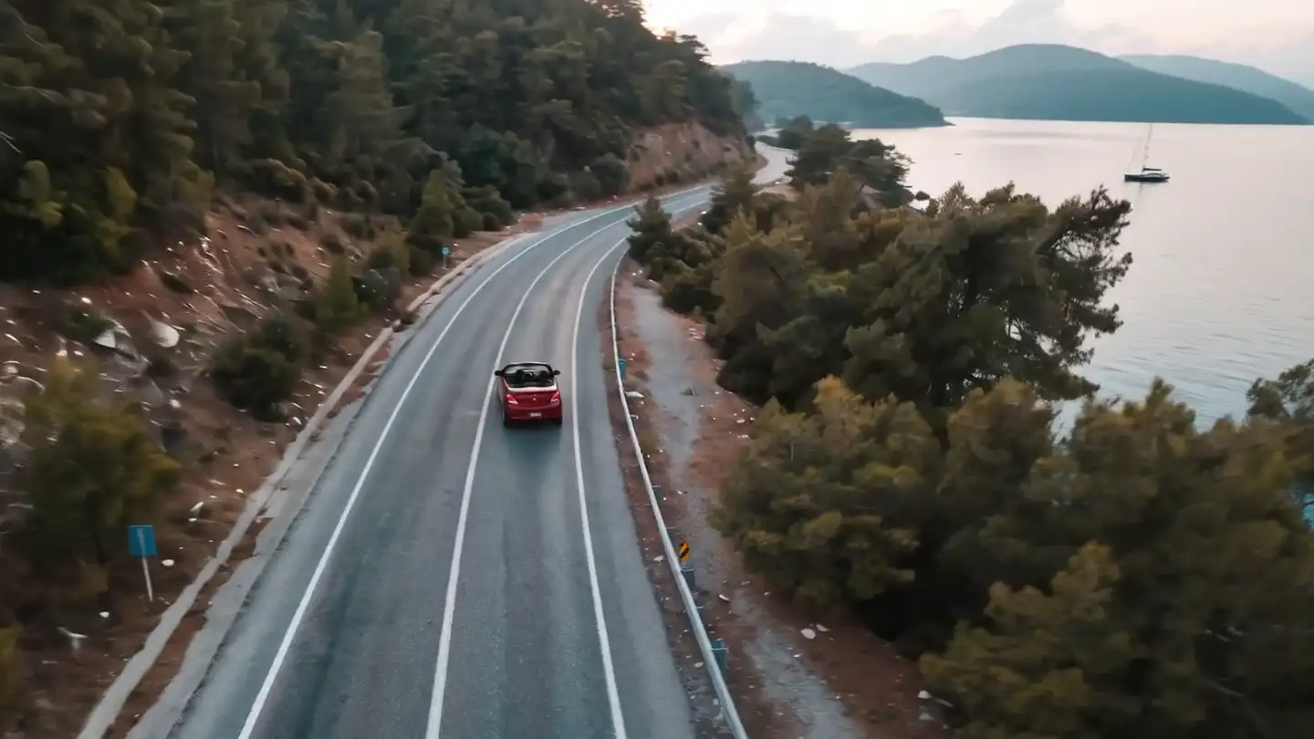 Fethiye kıyı yolunda üstü açık kırmızı otomobil, arkada turkuaz koy (temsili)